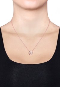 Roseguld halskæde med en blomsterpendant på en delikat kæde, præsenteret mod en sort top og en neutral baggrund.