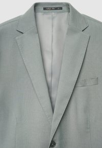 Hellgrauer Blazer mit strukturierter Oberfläche, zwei Vordertaschen und einem Einzelknopfverschluss. Das Innenfutter ist glatt und mit einem Etikett versehen.