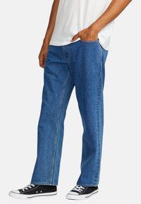 Blå denimjeans med lige snit, med en mellem-høj talje, synlige sømme og sidelommer. Båret med sorte kanvas sneakers.