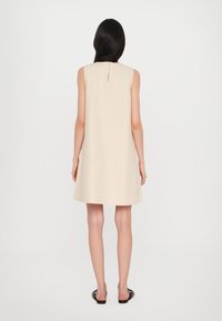 Vestido sin mangas de color beige con un corte relajado, hasta la rodilla, que presenta un detalle de ojal en la espalda y una tela suave y ligera.