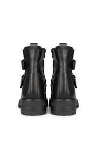 Botas de cuero negras hasta el tobillo con una suela gruesa, cremalleras laterales y hebillas ajustables a los lados. Textura suave con detalles mínimos.