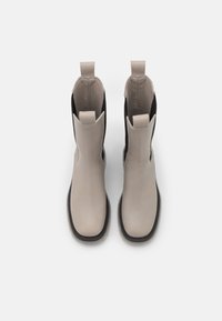 Stivali ankle in pelle beige con lati elastici neri, linguette per il trascinamento e suole in gomma testurizzata. Design elegante e moderno con forma affusolata.