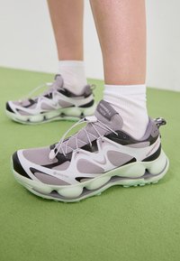 Baskets de sport GORE-TEX violet clair avec une tige en maille texturée, des accents noirs et une semelle sculptée. Comprend des lacets élastiques et un col rembourré.