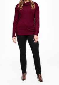 Bordowy sweter z kapturem i luźnym krojem, długimi rękawami oraz prążkowanym wykończeniem, zestawiony z czarnymi obcisłymi spodniami i brązowymi, wzorzystymi botkami za kostkę.