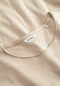 Beige, lightweight fabric t-shirt with a round neckline, featuring subtle texture and a GABBA label at the collar.