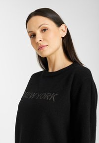 Zwarte trui met een ronde halslijn, met een getextureerde "NEW YORK" opdruk op de borst. Zacht materiaal met een comfortabele pasvorm.