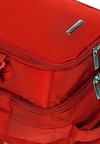 Bolsa de tela roja con dos compartimentos con cremallera, superficie texturizada y un logotipo metálico. Incluye un distintivo detalle de clip redondo.