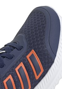 Zapato deportivo masculino con parte superior de malla en color navy, acentos en naranja, suela blanca y cordones negros. Superficie texturizada y acolchado para mayor comodidad.