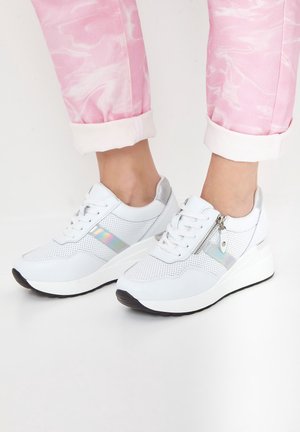 Weiße Plateausneaker mit irisierendem seitlichem Streifen und Reißverschluss-Detail, getragen mit hochgekrempelten rosa Batikhosen.