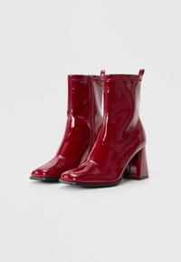 Bottes de cheville en vernis rouge avec un talon carré haut, dotées d'une fermeture éclair à l'avant et d'une surface lisse et brillante.
