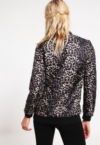 Veste bomber en imprimé léopard noir et beige, texture matelassée, bords-côtes aux poignets et à l'ourlet, design ajusté, vue de dos montrant le matériau léger.
