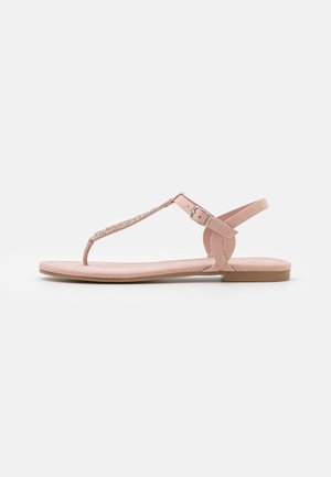 Flache rosa Damensandale mit dünnem Zehensteg, geschmücktem T-Riemen, verstellbarem Knöchelriemen und weicher Sohle auf weißem Hintergrund.