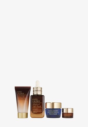 Quatre produits de soins de la peau Estee Lauder : un tube de crème marron, un flacon compte-gouttes avec un capuchon doré, un pot bleu avec un couvercle doré, et un petit pot marron.