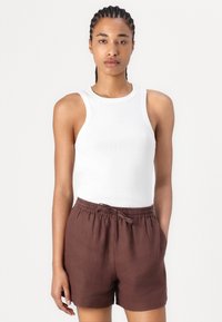 Un débardeur blanc à côtes associé à un short en lin marron avec une taille élastique et un cordon de serrage, sur un fond clair uni.