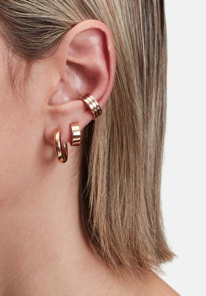 Drei Ohrhänger aus Roségold, die am Ohr präsentiert werden: ein großer glatter Ring, ein kleiner polierter Ring und ein gestreifter Band.