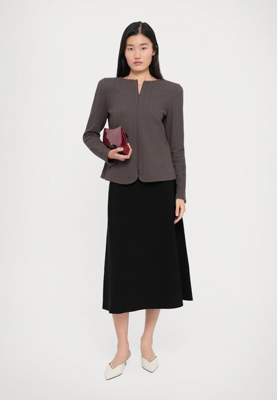 Brown houndstooth-patterned blazer with a rounded collar, paired with a black midi skirt. Model holds a small red purse and wears cream mules.