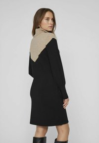 Robe en tricot noire avec un détail en chevrons beige au niveau du col, des manches longues et des poignets côtelés, présentant une coupe décontractée et une longueur jusqu'aux genoux.