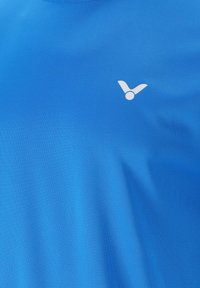 Blå sportskjorte med korte ærmer lavet af glat, letvægtsstof; har et hvidt logo på venstre side af brystet.