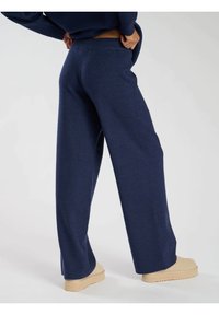Pantaloni a gamba larga navy realizzati in morbido tessuto a maglia, con una vita alta e una superficie liscia, abbinati a scarpe beige slip-on.