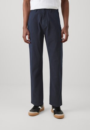 Dark blue, straight-leg pants made of cotton twill fabric. Features a classic waistband and side pockets. Paired with black sneakers.