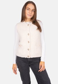 Elfenbeinfarbener, flauschiger Weste mit rundem Halsausschnitt, fünf dekorativen Knöpfen und zwei vorderen Taschen, getragen über einem weißen Langarmshirt.