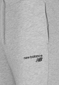 Světle šedé tepláky s jemnou texturou, na levé straně se černým logem "new balance" a elastickým pasem.