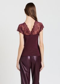 Top bordeaux con maniche a capfall in pizzo e design a V sulla schiena. Materiale morbido con una silhouette aderente, abbinato a pantaloni coordinati ad alta lucentezza.