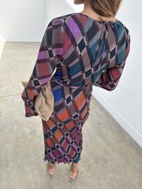 Rochie în carouri multi-colore, cu textură pliată, mâneci lungi și detaliu cu fundiță în spate. Asortată cu o poșetă bej și sandale cu curele.