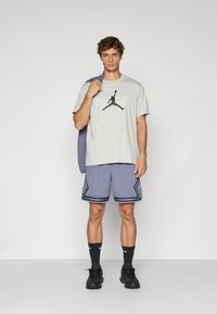 Camiseta de algodón gris con logo gráfico negro, combinada con pantalones cortos deportivos azules perforados con ribetes y acentos negros. Zapatillas negras y calcetines.