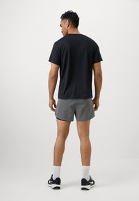 Conjunto atlético para hombre que incluye una camiseta de manga corta negra y pantalones cortos grises. La camiseta es suave, los pantalones cortos son ligeros, con un diseño elegante y colores neutros.