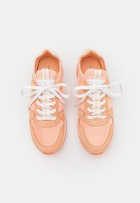 Tenisky s měkkou broskvovou tkaninou a semišovým svrškem, bílé tkaničky a živé oranžové podrážky. Text na jazyku zobrazuje název zna�čky.