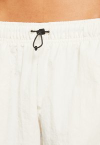 Bílé šortky s elastickým pasem a šňůrkou na stahování, s černými detaily, vyrobené z lehké strukturované látky.