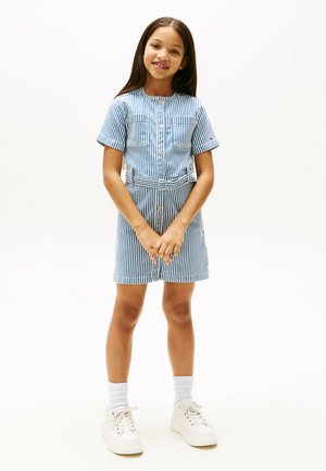 Vestido de rayas azul y blanco de manga corta con botones en el frente, dos bolsillos en el pecho y un cinturón en la cintura, combinado con zapatillas blancas y calcetines cortos.
