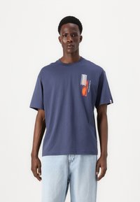 Námořnická modrá bavlněná tričko s krátkými rukávy, s abstraktním potiskem v oranžové a bílé na levé části hrudi. Klasický design s kulatým výstřihem.