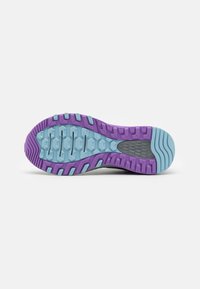La suela de la zapatilla de trail presenta un agarre texturizado con acentos en púrpura y azul claro, incorporando patrones hexagonales y una sección central gris.