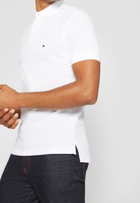 Vit polo-tröja med krage, kort ärm och en liten logotyp på vänster bröst. Matchad med mörka denimjeans.