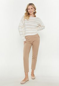Gehaakt sweater in crème met beige strepen, gecombineerd met beige slim-fit broeken en zachte beige ballerina's. Heeft losse mouwen en een ronde hals.