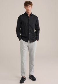 Črna srajca s kragnjo, v kombinaciji s svetlo sivo karirasto hlačami in črnimi loafers čevlji. Srajca ima klasičen ovratnik in eleganten kroj.