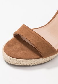 Bruine suède wedge sandaal met een brede bovenband en een geweven jute platform. Glad interieur en een gestructureerde buitenzool voor grip.