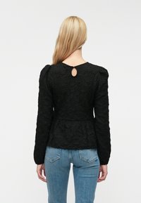 Czarna fakturowana bluzka z długimi rękawami i dekoltem w kształcie łezki, z marszczonym pasem, w połączeniu z jasnoniebieskimi dżinsami.