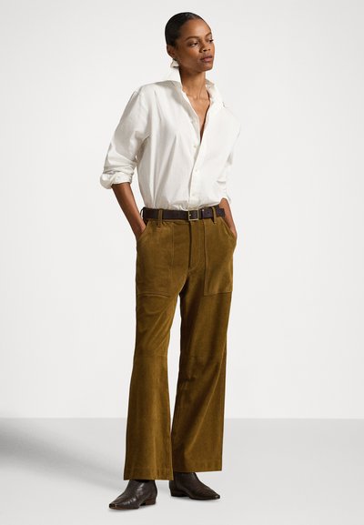 Bijela košulja s dugim rukavima urolanim do laktova, smeđe široke hlače od korduroga i crne gležnjače. Smeđi kožni remen s kopčom.