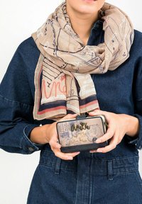 Beige Schal mit abstraktem Muster, der um eine Jeansjacke gewickelt ist. Eine gemusterte Geldbörse mit einem schwarzen Grund, die in den Händen gehalten wird und ein verspieltes Design aufweist.