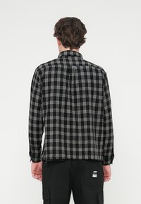 Ανδρικό πουκάμισο με καρό μοτίβο σε ασπρόμαυρο, με γιακά που κουμπώνει, μακριά μανίκια και ευθεία τελείωμα. Διαθέτει υφή υφάσματος και λεπτομέρεια ετικέτας στην τσέπη.