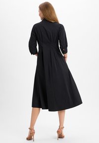 Black midi dress with three-quarter sleeves, fitted bodice, and pleated skirt. Made from smooth fabric with a collar and back button detail.