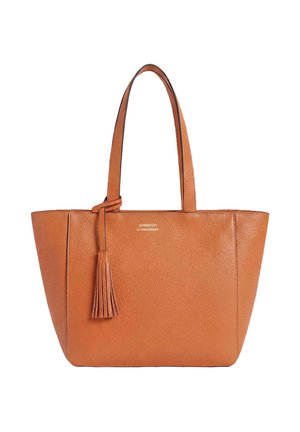 Sac cabas en cuir marron avec deux poignées et un pompon décoratif suspendu à une poignée, surface texturée visible.