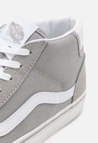 Zapatillas de lona grises con una franja lateral de cuero blanco, acentos de ante gris texturizado, cordones planos blancos y un cuello acolchado en el tobillo.