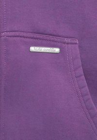 Lila Kapuzenpulli mit einer Fronttasche und einem silbernen Logoschild mit der Aufschrift "basic republic". Glattes Material mit sichtbaren Nähdetails.