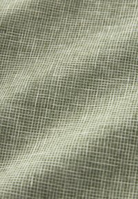 Gros plan sur un tissu vert avec un motif à grille blanche montrant une texture douce et des plis subtils.