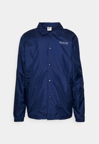 Navy blue, lightweight, waterproof jacket with a pointed collar, snap buttons, and "PARIS" logo on the left chest. Features elastic cuffs.