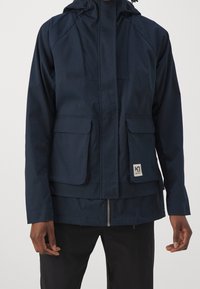 Navy blue waterproof jacket with adjustable hood, two front flap pockets, and a zipper, featuring a logo patch on the lower left.